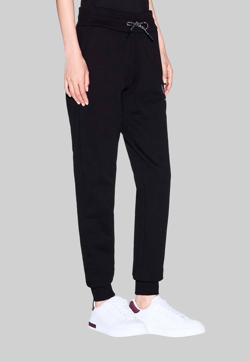 Zwarte joggers met een geribbelde tailleband en trekkoord, met zijzakken en taps toelopende boorden. Gecombineerd met witte sneakers.