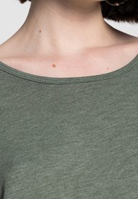 Oliivinvihreä, ribbineuloksinen kangastoppi, jossa leveä pääntie ja pehmeä tekstuuri, esittelee puhtaan, yksinkertaisen muotoilun ja hienovaraiset vaakasuorat linjat.