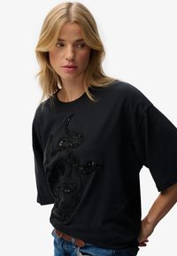 Camiseta de algodón negra con corte holgado, que presenta un diseño de calavera y serpiente negro brillante, mangas cortas y cuello redondo.