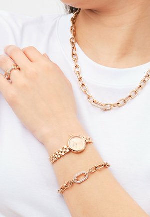 Rose gold wristwatch with a round face and linked band, paired with a textured chain bracelet. Simple ring also visible on the hand.