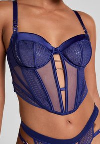 Navy blauwe lingerie van satijn en gaas, met een gestructureerd korsett ontwerp, kanten accenten en details in goudkleurige hardware.