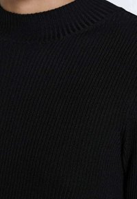 Maglione nero a coste con colletto alto e strutturato. La texture è liscia con linee verticali, sottolineando un design aderente.
