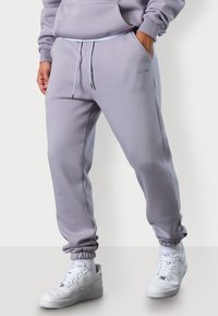 Helllila Jogginghose aus weichem Material mit elastischem Bund und Bündchen. Mit Seitentaschen und dezentem Logodetail. Kombiniert mit weißen Sneakers.