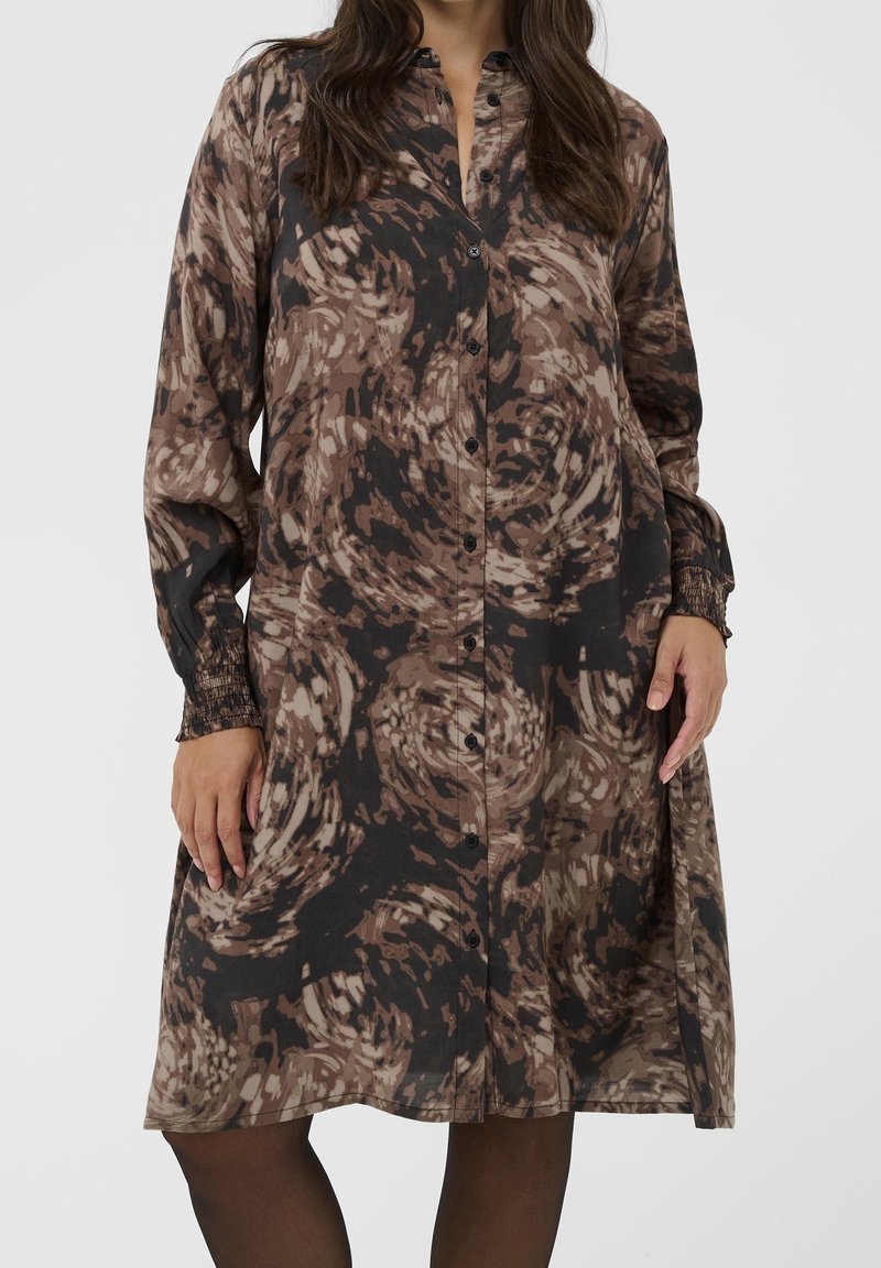 Femme portant une robe à manches longues boutonnée avec un motif abstrait tourbillonnant marron et noir et des poignets élastiqués.