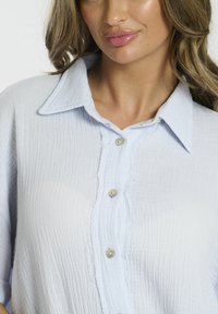 Lichtblauwe button-up shirt van gestructureerde stof. Voorzien van een klassieke kraag, drie knopen en een licht rafelige rand.