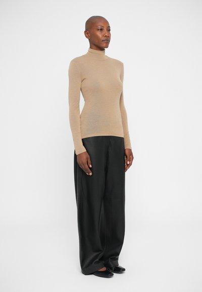 Pulover bej, ajustat, cu guler înalt dintr-un material moale, cu mâneci lungi. Asortat cu pantaloni negri largi, creând un look minimalist.