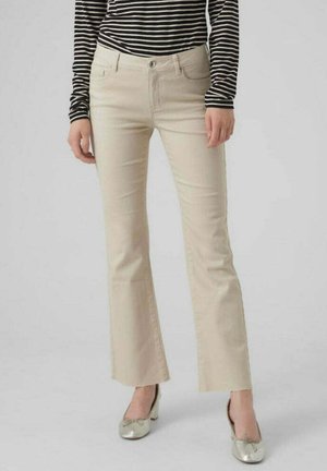Jeans beige a zampa d'elefante con vita media, dotati di tasche frontali e una texture liscia, abbinati a scarpe metalliche e maniche lunghe a righe.