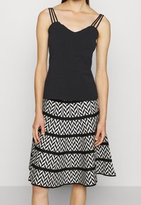 Top nera senza maniche con scollo a V e spalline sottili, abbinato a una gonna a strati con un motivo zigzag bianco e nero.