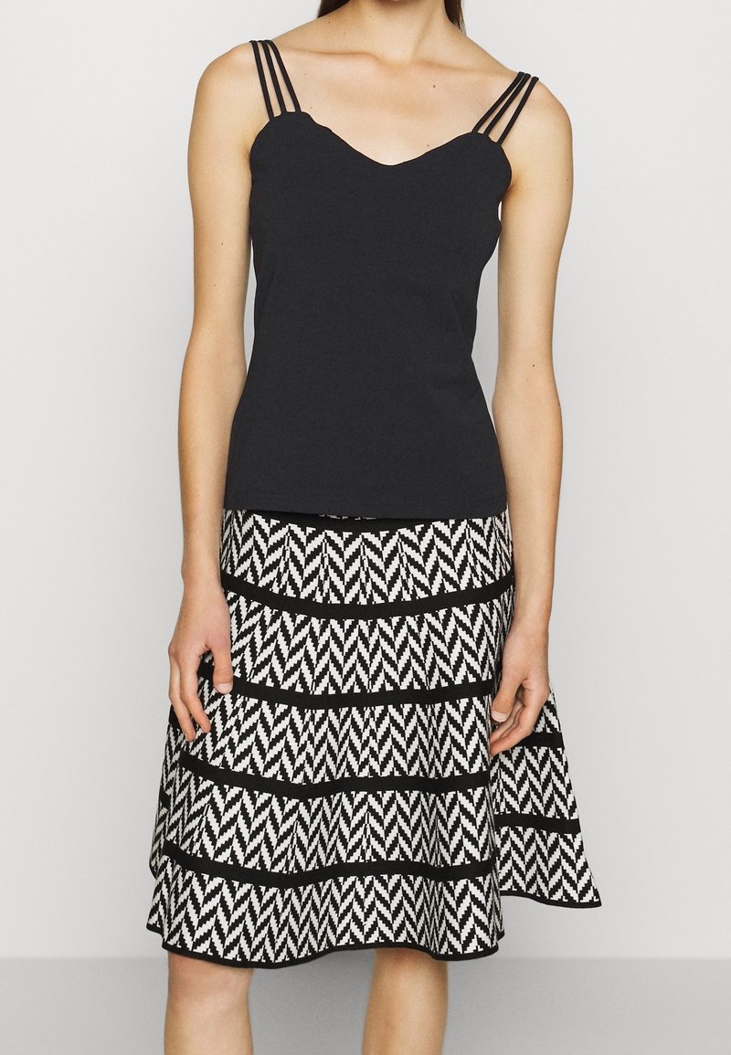 Top nera senza maniche con scollo a V e spalline sottili, abbinato a una gonna a strati con un motivo zigzag bianco e nero.