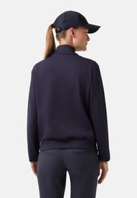 Námořnická mikina s vysokým límcem, dlouhými rukávy a hladkou texturou, v kombinaci se stejnobarevnými námořnickými kalhotami a kšiltem.