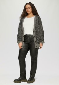 Grauer Cardigan mit strukturiertem Muster, Knopfverschluss und kontrastierendem helleren Besatz, kombiniert mit schwarzen Lederhosen und klobigen schwarzen Stiefeln.