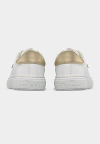 Λευκά αθλητικά παπούτσια με λεία επιφάνεια, διακοσμημένα με μεταλλική χρυσή λεπτομέρεια στη φτέρνα και υφασμένη λευκή καουτσούκ σόλα με ανάγλυφο το όνομα της μάρκας.