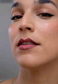 Close-up van een gezicht met gladde huid, gedefinieerde jukbeenderen, een subtiele roze lipkleur en opvallende eyeliner op het bovenste ooglid.