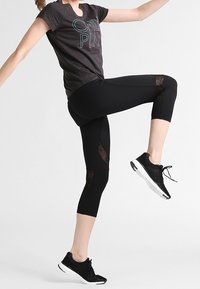 Black athletic leggings with mesh panels, paired with a short-sleeve dark gray T-shirt featuring colorful text, and black running shoes.