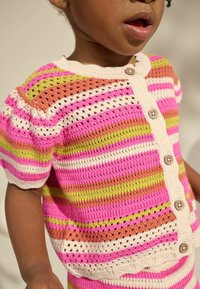 Cardigan lavorato a maglia multicolore con strisce rosa, bianche, verdi e arancioni; presenta maniche corte a sbuffo e bottoni in legno sul davanti.