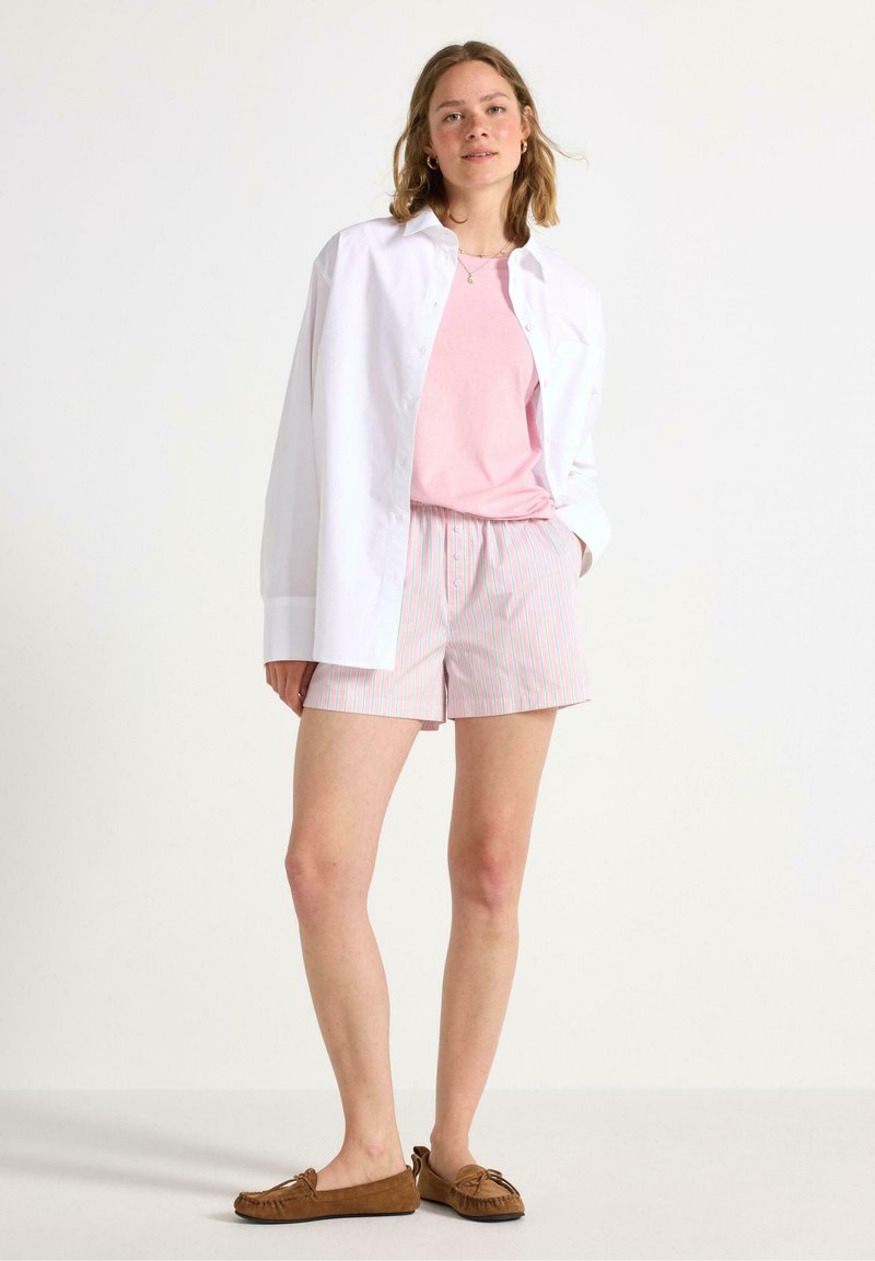 Lyserød t-shirt, oversized hvid skjorte med knapper, stribede shorts med pink og blå linjer, og brune slip-on mokkasiner.