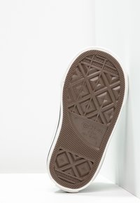 Brązowa gumowa podeszwa z geometrycznym wzorem bieżnika, białe boki oraz tłoczone logo "Converse All Star" na spodzie.