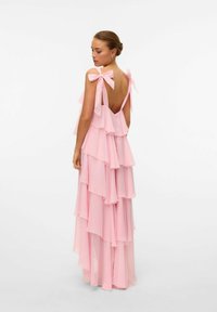 Abito in chiffon rosa con strati arricciati, schiena scoperta e fiocchi sulle spalline. Tessuto leggero con un design fluido.