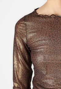 Long-sleeve top in brown with a leopard print design, featuring metallic gold accents and a scalloped neckline. Smooth texture.