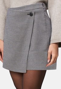 Svart och vit houndstooth omslagsskjorta med sidoknappar och veck. Tillverkad av vävt tyg med en mjuk textur.
