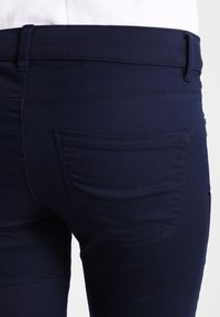 Navy modré strečové džínsy z bavlny s přiléhavým střihem, s kapsou na zadní straně a hladkou texturou, zobrazené ze zadu.