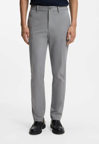 Szare spodnie garniturowe o dopasowanym kroju, z szlufkami na pasek, zapięciem na guzik z przodu oraz bocznymi kieszeniami. Noszone z czarnymi mokasynami.