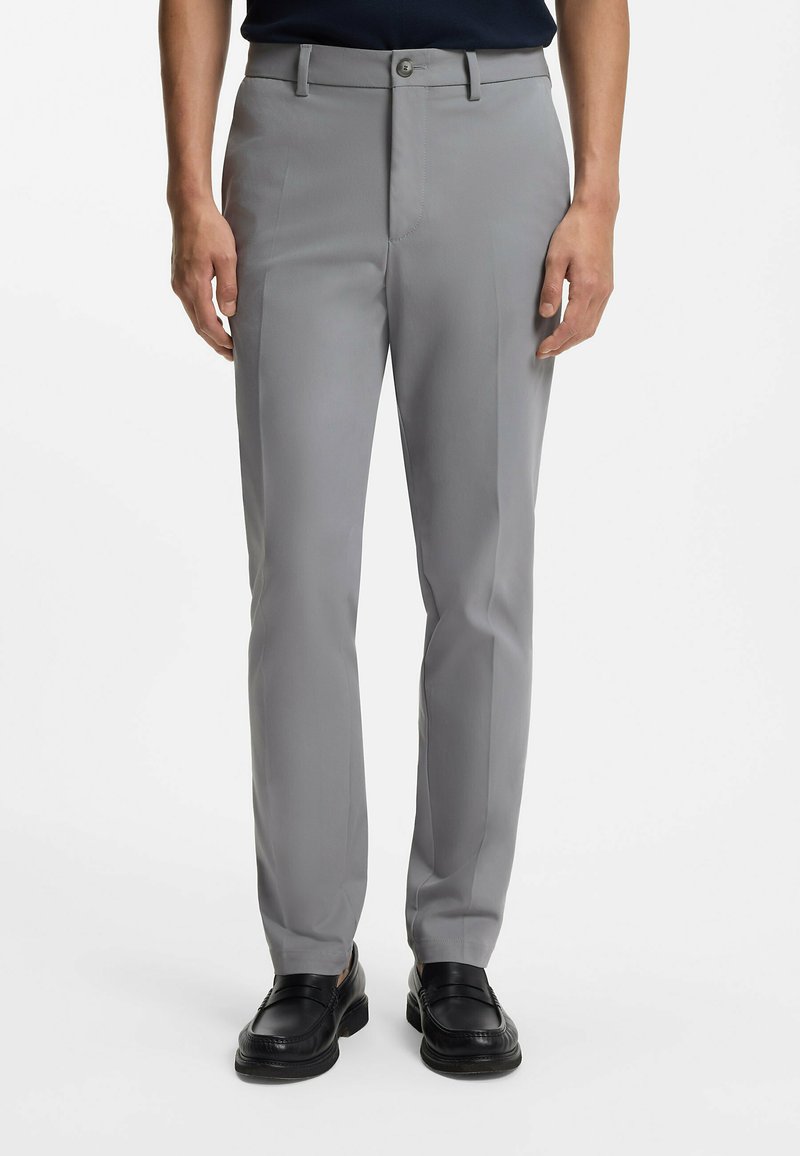 Szare spodnie garniturowe o dopasowanym kroju, z szlufkami na pasek, zapięciem na guzik z przodu oraz bocznymi kieszeniami. Noszone z czarnymi mokasynami.