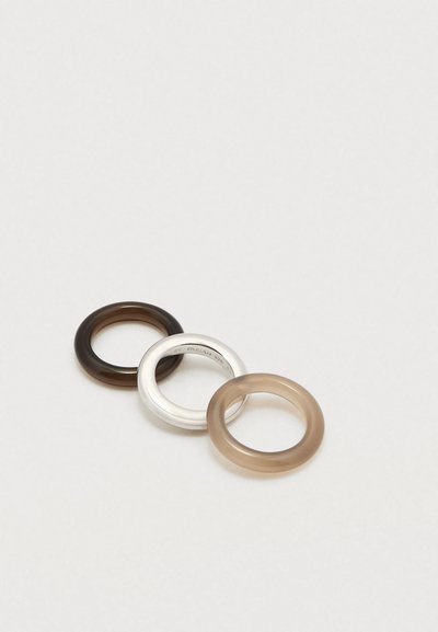 Trois anneaux : un brun foncé, un argenté avec gravure, et un brun clair. Texture lisse, forme circulaire, transparences variées.