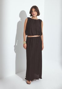 Musta plisattu lyhyt toppi ja pitkä hame, joissa on löysä istuvuus ja pehmeä rakenne. Mukana kultainen rannekoru. Minimalistinen muotoilu.