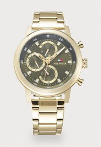 Montre-bracelet en métal doré avec un cadran sombre, trois sous-cadrans indiquant les jours, l'heure sur 24 heures et les secondes, ainsi que le logo Tommy Hilfiger sur le cadran.