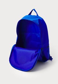 Mochila azul feita de tecido, com um grande compartimento principal, dois bolsos laterais com fecho éclair e uma alça na parte superior para transporte.
