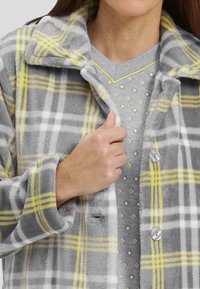 Chaqueta de franela a cuadros grises con rayas amarillas y blancas, gran cuello y botones plateados, superpuesta sobre una blusa de patrón gris claro.