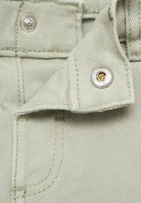 Țesătură de un verde deschis cu un finisaj texturat, având un buton metalic cu capcană și detalii de cusătură, evidențiind un colț pliat al articolului vestimentar.