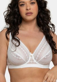 Soutien-gorge en dentelle blanche avec des motifs géométriques, une bordure texturée, des bretelles ajustables et un petit nœud en accent au centre. Tissu doux et léger.