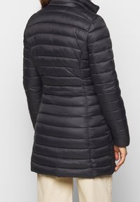 Schwarze Pufferjacke mit taillierter Silhouette, horizontalen Nähten, hohem Kragen und glatter Textur. Der Saum reicht bis zur Mitte des Oberschenkels für zusätzliche Wärme.