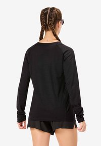 Zwart shirt met lange mouwen en raglanmouwen, zachte stof, ronde hals en zijsplitten, gecombineerd met donkere korte broek voor een atletische uitstraling.