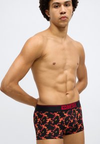 Boxershorts i svart bomull med et rødt blomsterprint, med en bred svart elastisk midjebånd med "DIESEL"-logoen i rødt.