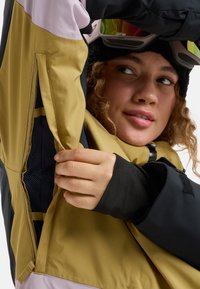 Schneejacke mit einem Farbblockdesign in Schwarz, Gold und Pink. Das Material scheint strapazierfähig zu sein, mit Netzfutter und verstellbaren Bündchen.