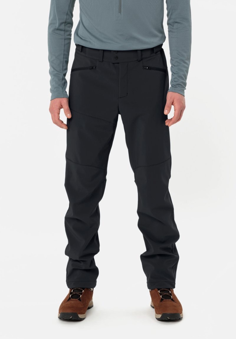 Svarta utomhusbyxor med skräddarsydd passform, med dragkedjor på fickorna och förstärkta knän. Kombineras med en grå långärmad tröja och bruna stövlar.