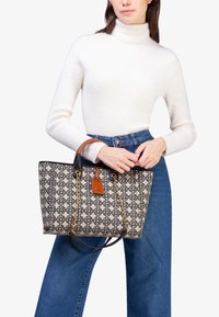 Borsa a tracolla con un motivo geometrico in beige e blu navy, manici in pelle nera, dettagli in catena dorata e un'etichetta in pelle marrone.