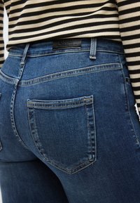 Σκούρο μπλε τζιν μεσαίας μέσης, με πίσω τσέπες και ραφές, συνδυασμένο με μπλούζα με ασπρόμαυρες ρίγες.