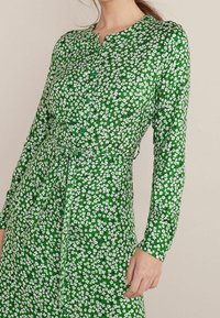 Robe verte à motif floral, dotée de longues manches, d'un col rond, de boutons sur le devant et d'une ceinture à nouer à la taille.
