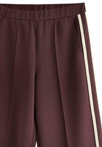 Pantaloni in misto poliestere bordeaux con vita alta, caratterizzati da strisce laterali bianche e tasche frontali, che presentano una texture liscia e un design sartoriale.