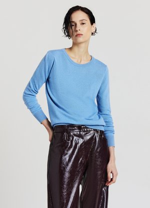Pull en maille bleu clair avec un col rond et des manches longues, associé à un pantalon bordeaux brillant. Texture douce et coupe ajustée.