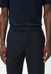 Pantalones marinos de corte slim, con trabillas para cinturón, cierre de botón y diseño de frente plano. Tela suave con un brillo sutil.
