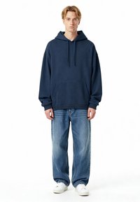 Felpa con cappuccio blu navy con tasca frontale, vestibilità comoda, polsini a coste, abbinata a jeans denim larghi azzurri e sneaker bianche.