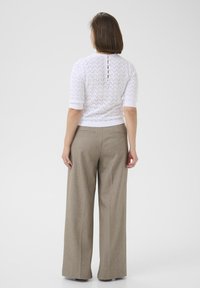 Maglione bianco a maglia con maniche corte e un motivo testurizzato, abbinato a pantaloni beige a gamba larga con vita alta, dotati di dettagli con bottoni posteriori.