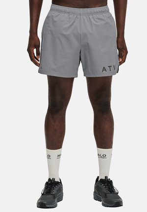 Shorts de sport gris avec une taille élastique, des poches latérales et le texte imprimé "ATV" sur la jambe gauche. Associés à des chaussures noires et des chaussettes blanches.