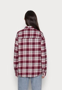 Rutigt flanellskjorta i burgundy och vitt, med en knapp-ned krage, långa ärmar och en rak nederkant med rundade kanter.