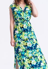 Kukallinen maksimekko, jossa on vihreitä, sinisiä ja valkoisia värejä. V-kaula-aukko, ilman hihoja oleva malli, elastinen vyötärö ja sivuaukot tarvittavaa ilmanvaihtoa varten.